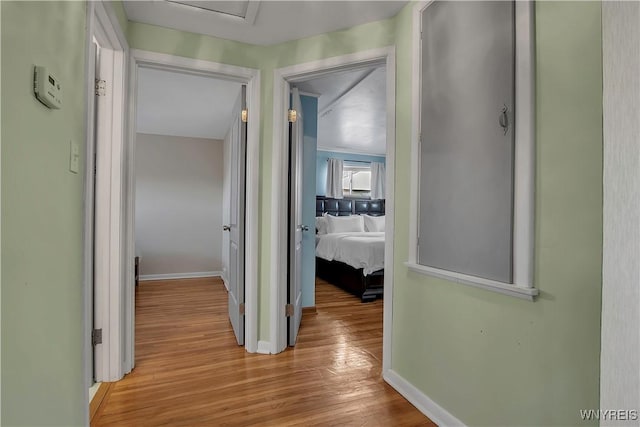 hall featuring attic access, baseboards, and light wood-style floors