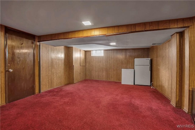 finished below grade area featuring carpet floors, wooden walls, and freestanding refrigerator