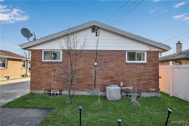 view of side of home with brick siding, a lawn, and fence