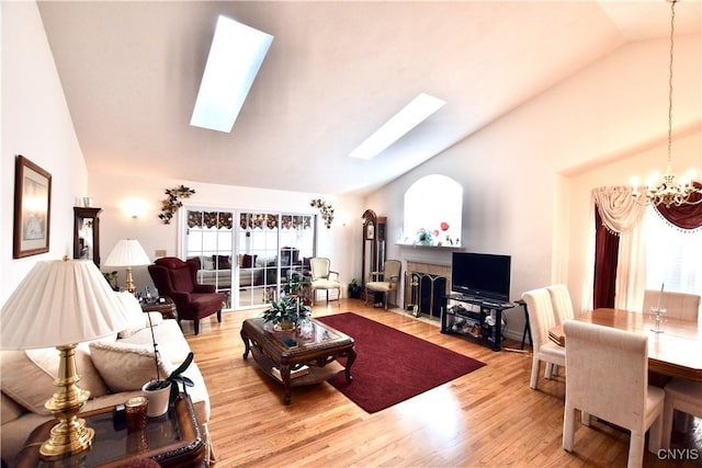 living room with high vaulted ceiling, a skylight, light wood-style floors, and an inviting chandelier