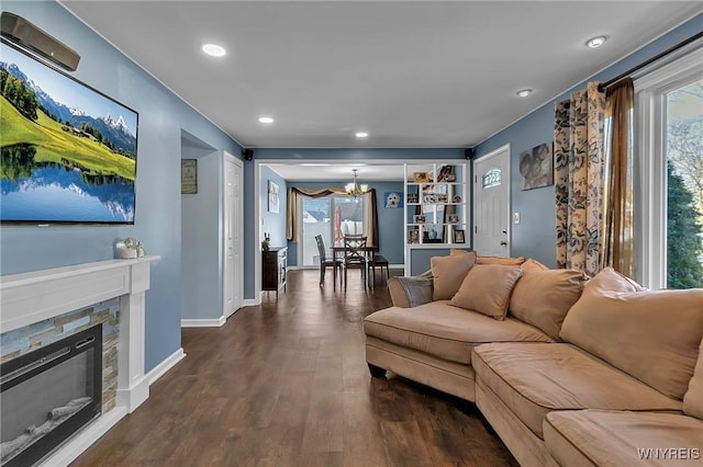 living room with plenty of natural light, a notable chandelier, a glass covered fireplace, and dark wood-style flooring