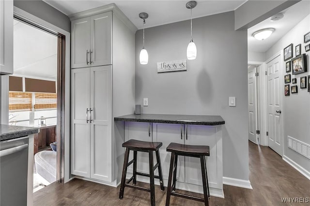 kitchen featuring visible vents, decorative light fixtures, a kitchen bar, stainless steel dishwasher, and dark wood-style flooring