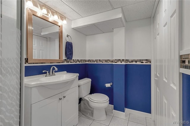 bathroom with tile patterned floors, toilet, a paneled ceiling, baseboards, and vanity