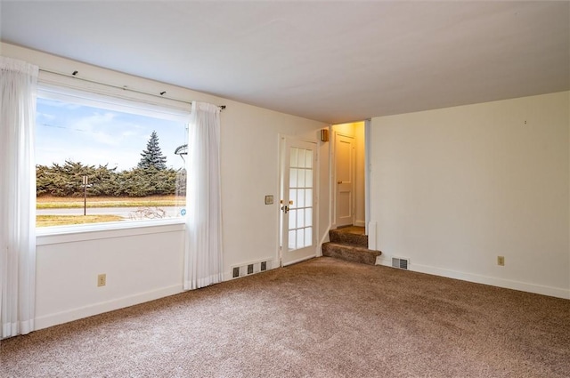 carpeted spare room with visible vents, stairs, and baseboards