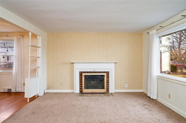 unfurnished living room with wallpapered walls, a brick fireplace, baseboards, and carpet floors