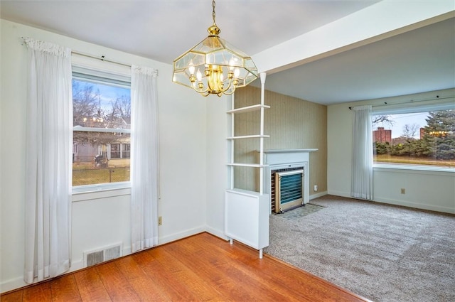 unfurnished living room featuring baseboards, visible vents, a fireplace with flush hearth, carpet flooring, and a chandelier