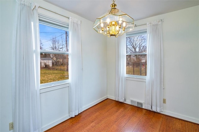 unfurnished dining area with visible vents, baseboards, an inviting chandelier, and wood finished floors