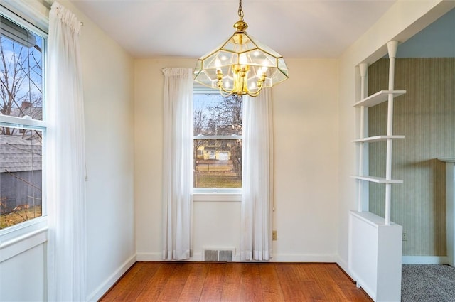 unfurnished dining area featuring visible vents, baseboards, a notable chandelier, and wood finished floors