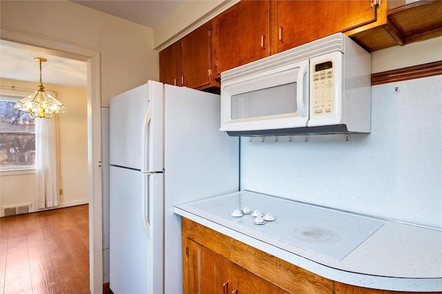 kitchen with visible vents, brown cabinets, white appliances, light countertops, and hanging light fixtures