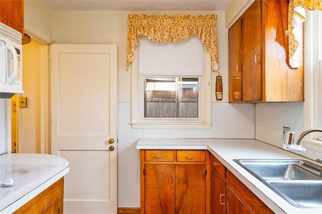 kitchen featuring a sink, brown cabinets, white microwave, and light countertops