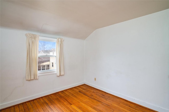 unfurnished room with baseboards, vaulted ceiling, and hardwood / wood-style flooring