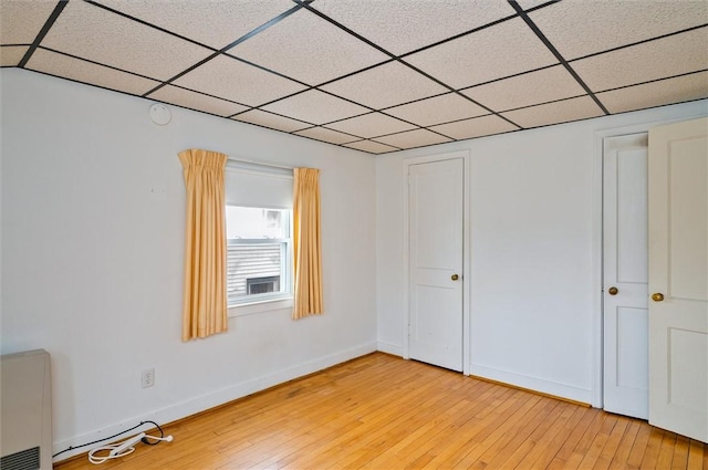 unfurnished bedroom with baseboards, a paneled ceiling, and light wood-style floors