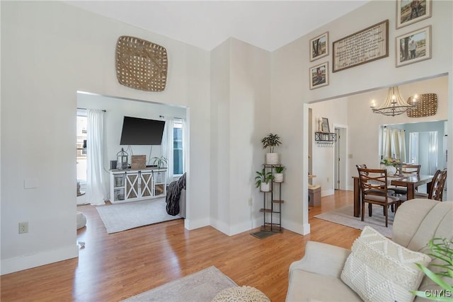 living area featuring baseboards, a high ceiling, an inviting chandelier, and wood finished floors