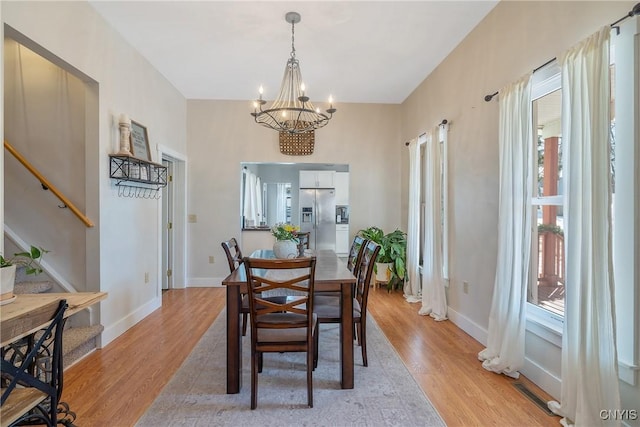 dining space with a notable chandelier, stairway, light wood-style flooring, and baseboards