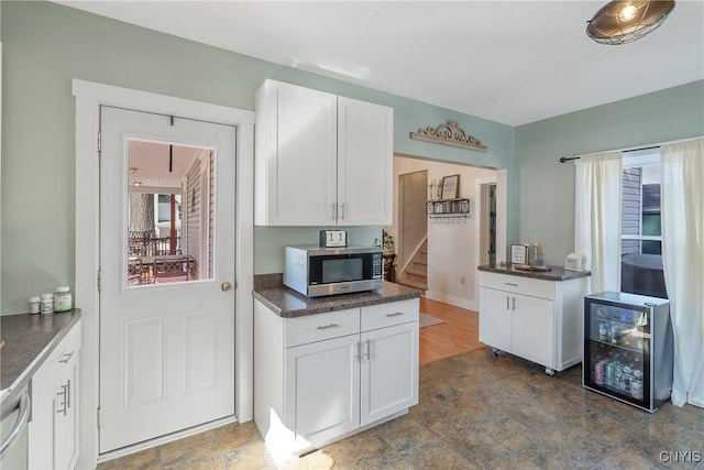 kitchen featuring white cabinetry, dark countertops, beverage cooler, and stainless steel appliances