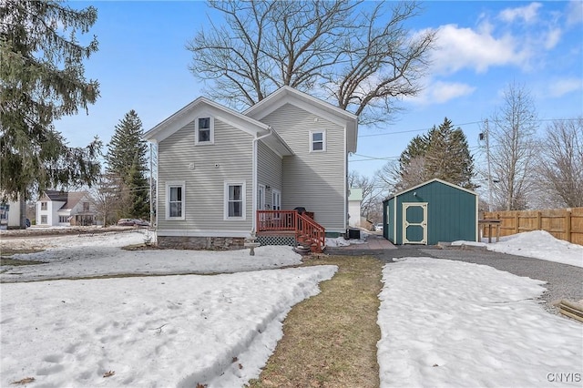 snow covered rear of property with a storage unit, a deck, fence, cooling unit, and an outdoor structure