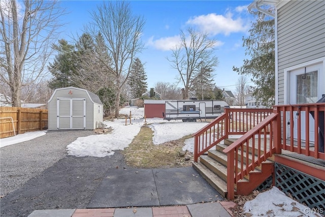 yard layered in snow featuring an outbuilding, a storage unit, a deck, and fence