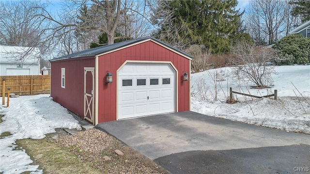 snow covered garage featuring a detached garage, fence, and aphalt driveway