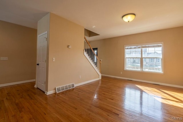 unfurnished living room featuring stairs, wood finished floors, visible vents, and baseboards