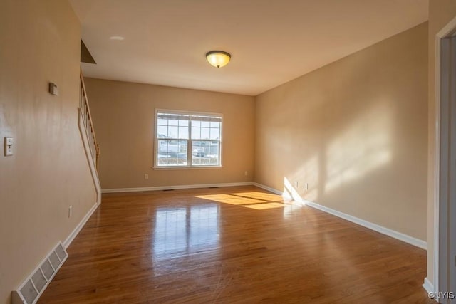 unfurnished room featuring visible vents, stairs, baseboards, and wood finished floors