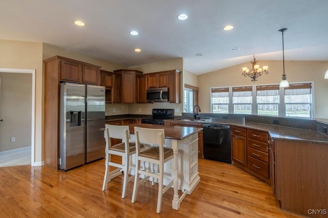 kitchen with a breakfast bar area, light wood finished floors, a peninsula, a sink, and black appliances