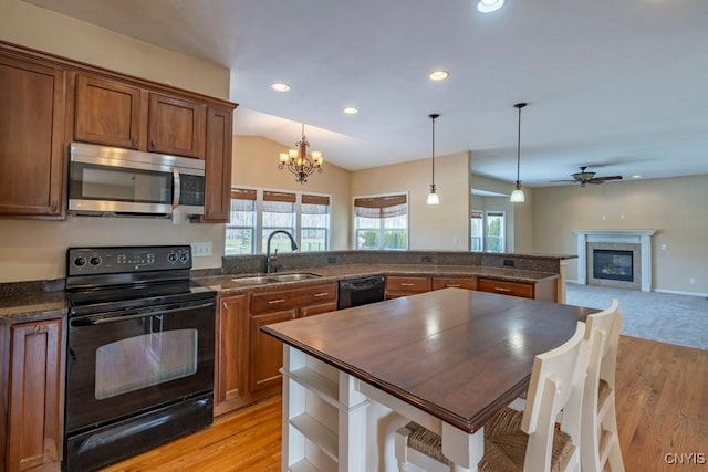 kitchen featuring open floor plan, a peninsula, a glass covered fireplace, black appliances, and a sink