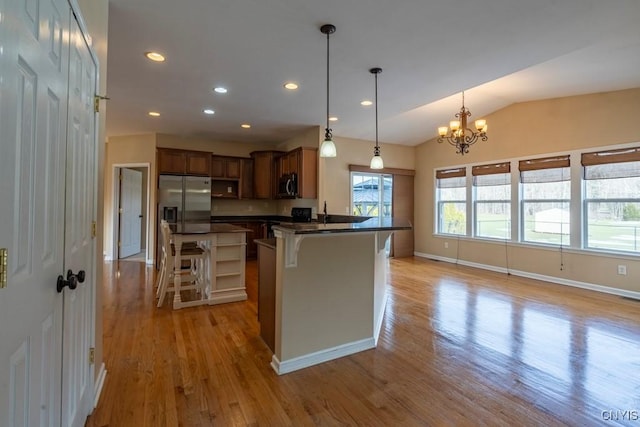 kitchen featuring light wood-type flooring, a breakfast bar, dark countertops, stainless steel appliances, and lofted ceiling