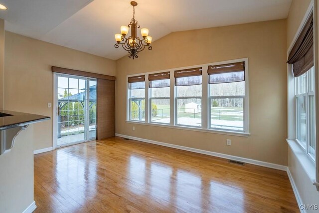 unfurnished dining area featuring visible vents, wood finished floors, baseboards, a chandelier, and vaulted ceiling