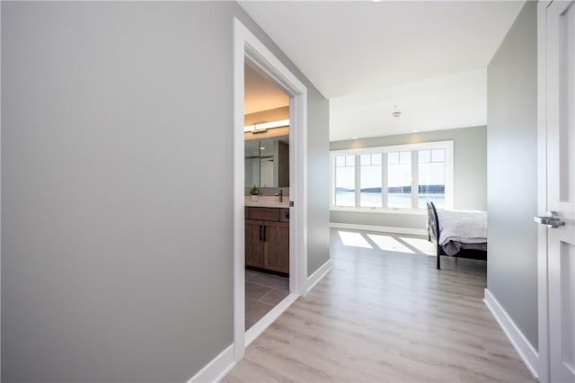 corridor featuring a sink, baseboards, and light wood-style floors