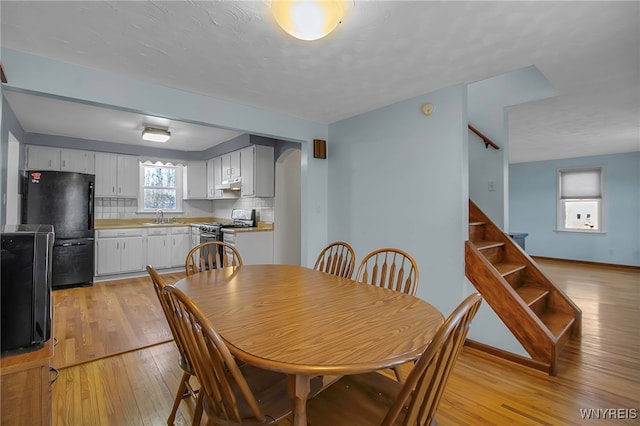 dining space with stairway, arched walkways, light wood-type flooring, and baseboards