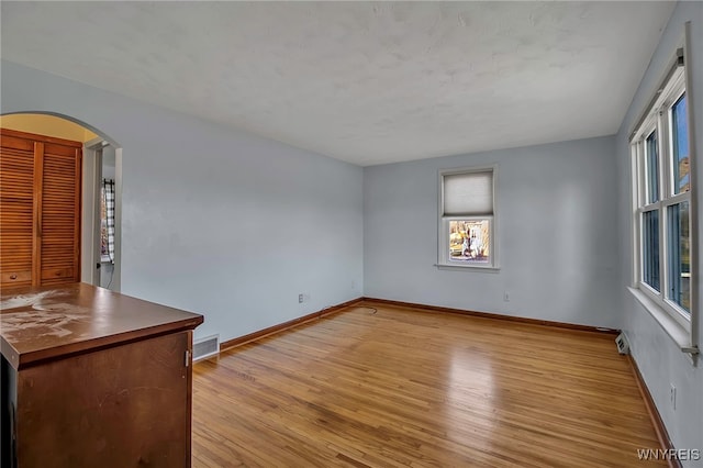 empty room with light wood-style floors, visible vents, arched walkways, and baseboards