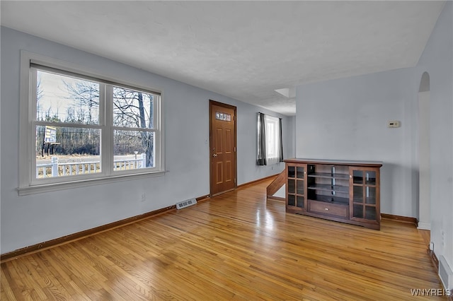 unfurnished living room featuring arched walkways, visible vents, baseboards, and light wood-style floors