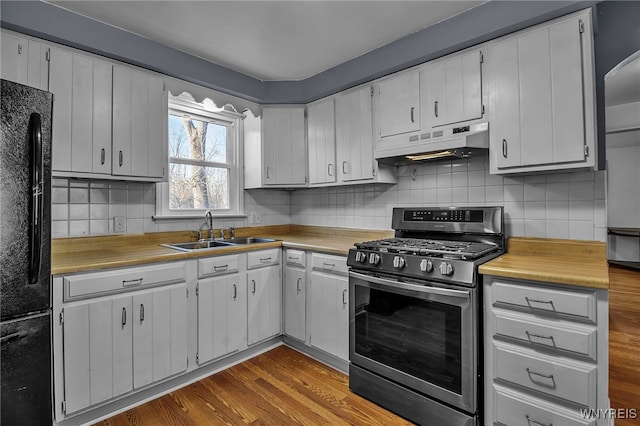 kitchen featuring under cabinet range hood, a sink, dark wood finished floors, freestanding refrigerator, and stainless steel range with gas stovetop