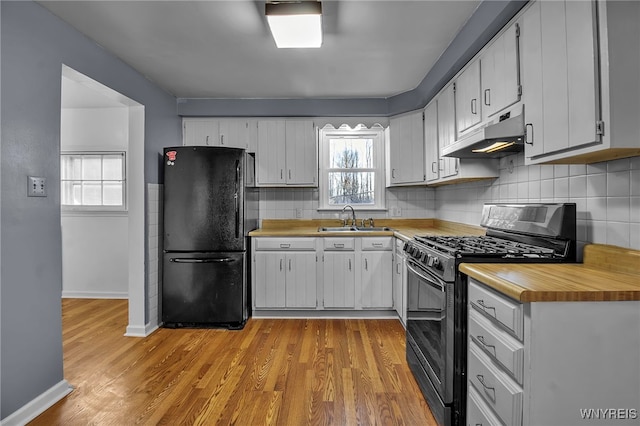 kitchen with light wood finished floors, under cabinet range hood, range with gas stovetop, freestanding refrigerator, and a sink