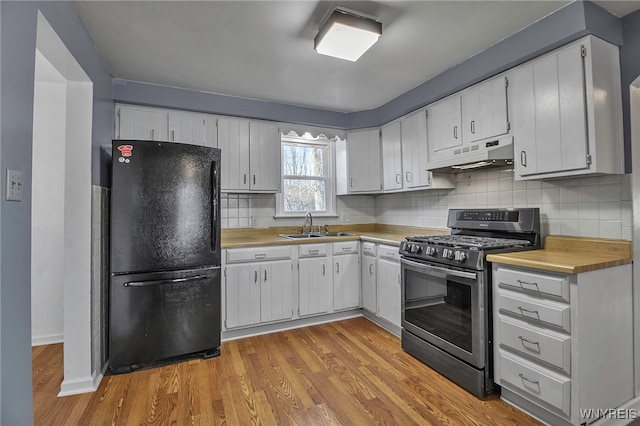 kitchen featuring under cabinet range hood, light countertops, freestanding refrigerator, stainless steel gas range, and a sink