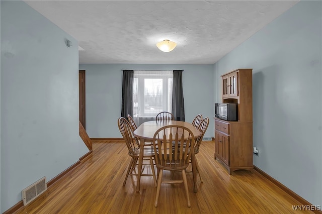 dining space featuring light wood-type flooring, visible vents, baseboards, and a textured ceiling