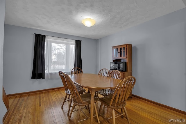 dining room featuring a textured ceiling, baseboards, and light wood-type flooring