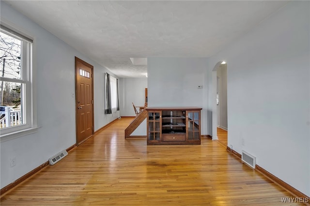 foyer entrance with light wood-style floors, arched walkways, visible vents, and baseboards