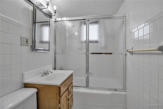 full bathroom with vanity, shower / bath combination with glass door, a textured ceiling, tile walls, and toilet