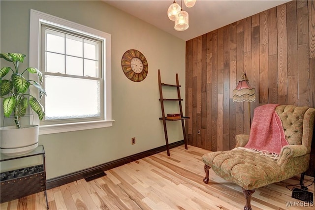 living area with light wood finished floors, wooden walls, baseboards, and visible vents