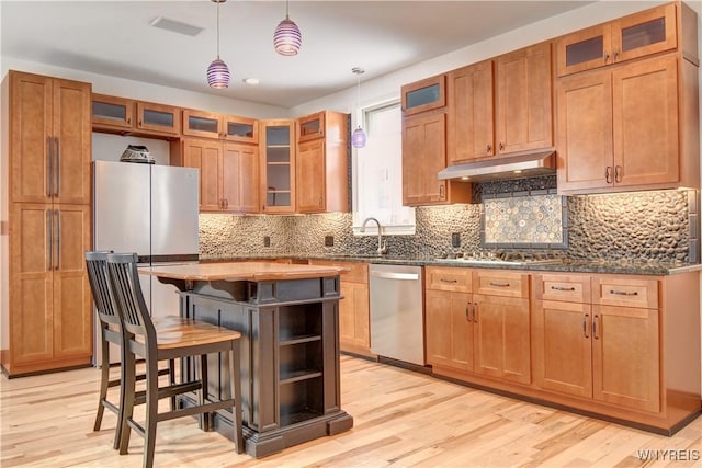 kitchen with pendant lighting, light wood-style flooring, under cabinet range hood, a center island, and appliances with stainless steel finishes