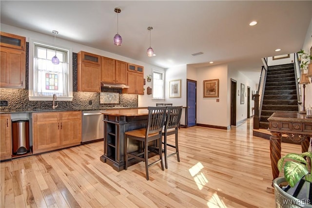 kitchen with brown cabinetry, backsplash, dishwasher, and a sink