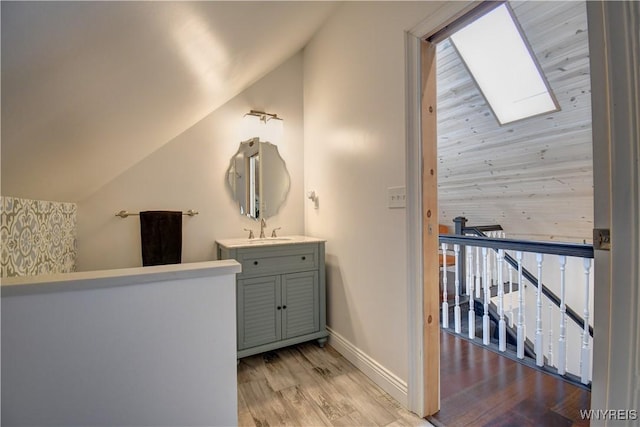 bathroom featuring baseboards, lofted ceiling with skylight, wood finished floors, and vanity