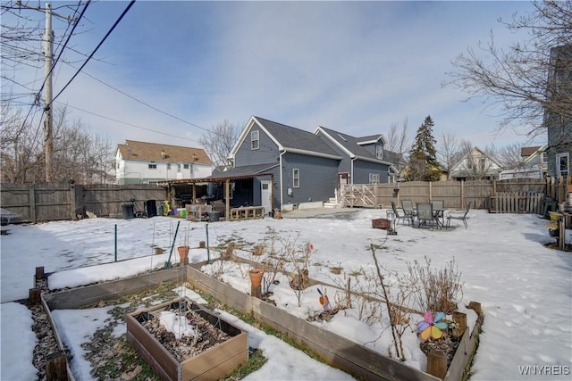 snow covered rear of property with a vegetable garden and a fenced backyard