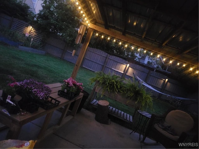 patio at night featuring a lawn and a fenced backyard