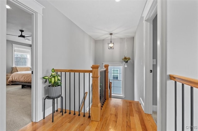 hall with wood finished floors, an upstairs landing, and baseboards