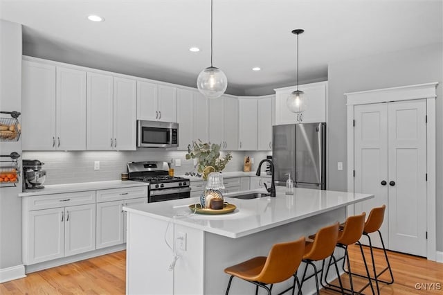 kitchen with light wood finished floors, a sink, white cabinets, appliances with stainless steel finishes, and a kitchen breakfast bar