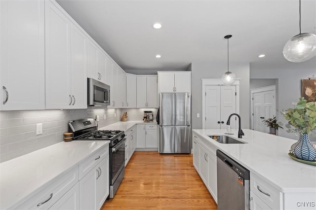 kitchen with a sink, appliances with stainless steel finishes, white cabinetry, light wood-type flooring, and backsplash