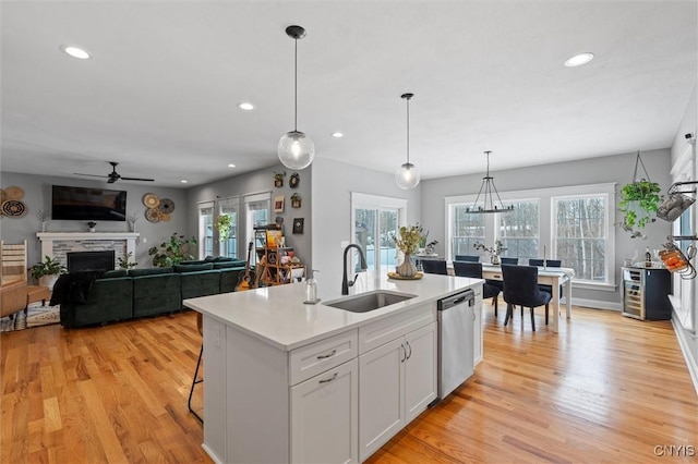 kitchen with light countertops, a stone fireplace, stainless steel dishwasher, light wood-style floors, and a sink