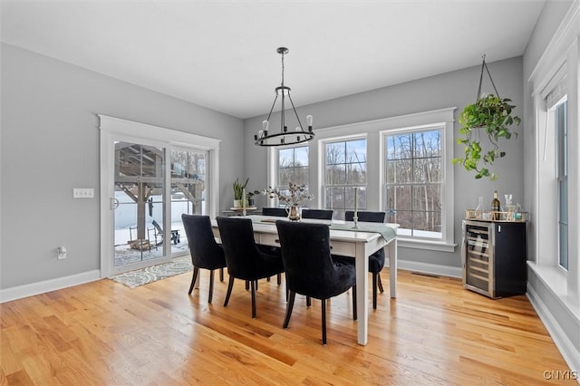 dining space with beverage cooler, baseboards, light wood-type flooring, and a chandelier